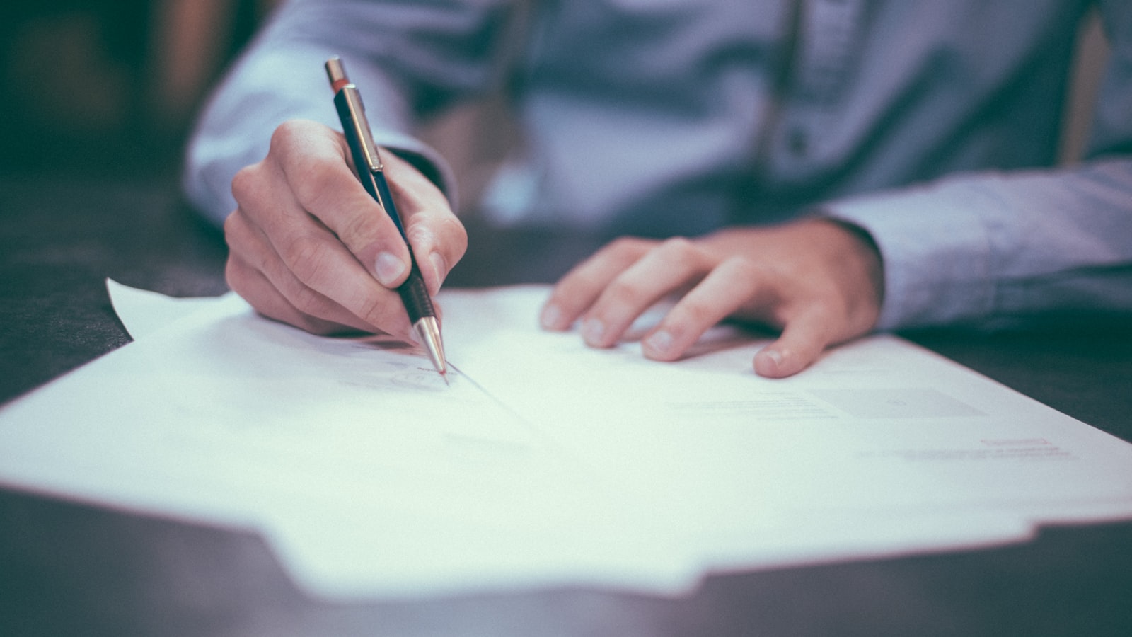 Hand signing a paper document with a black pen