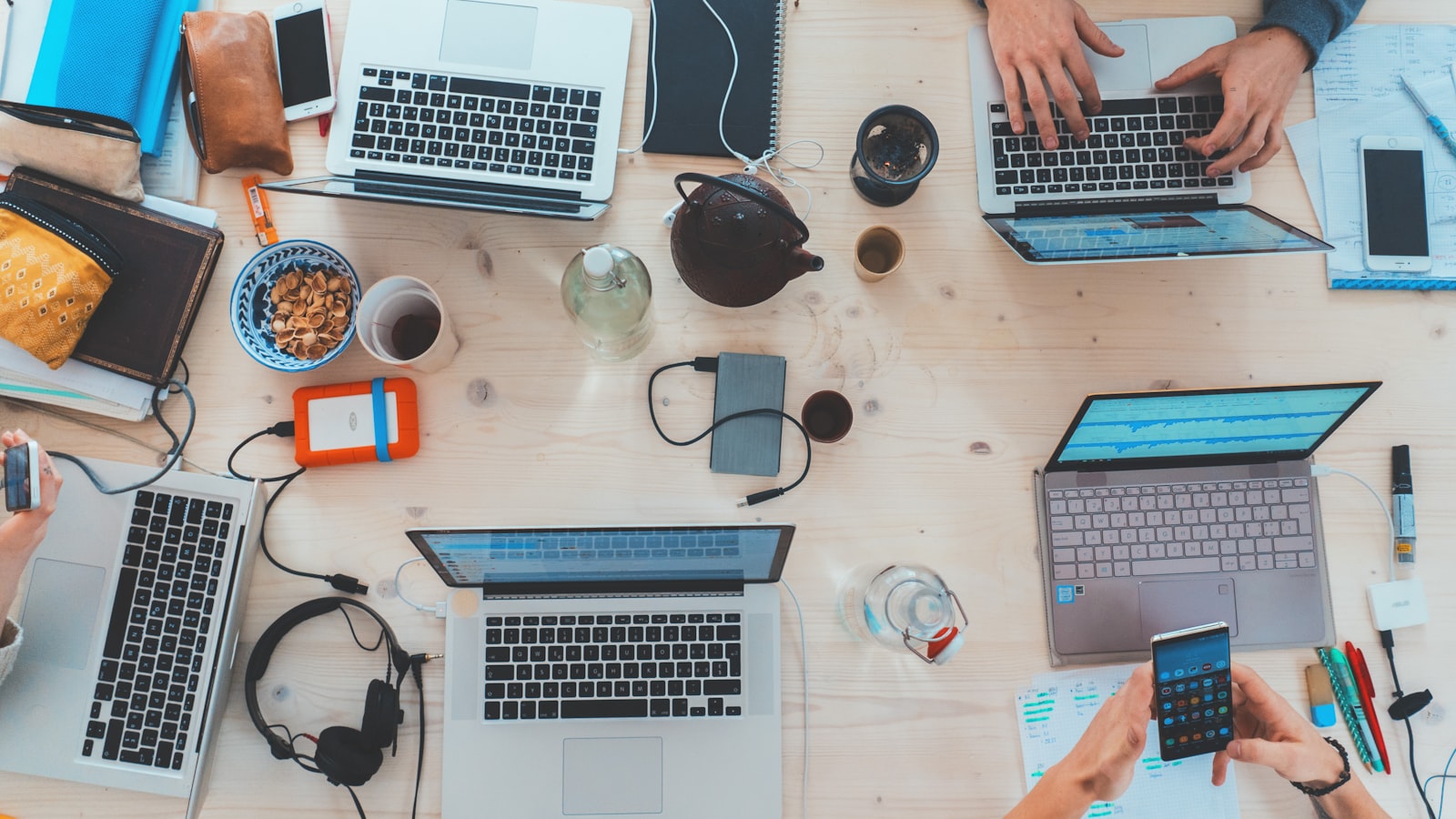 Several open laptops and notebooks spread across a long shared wooden table