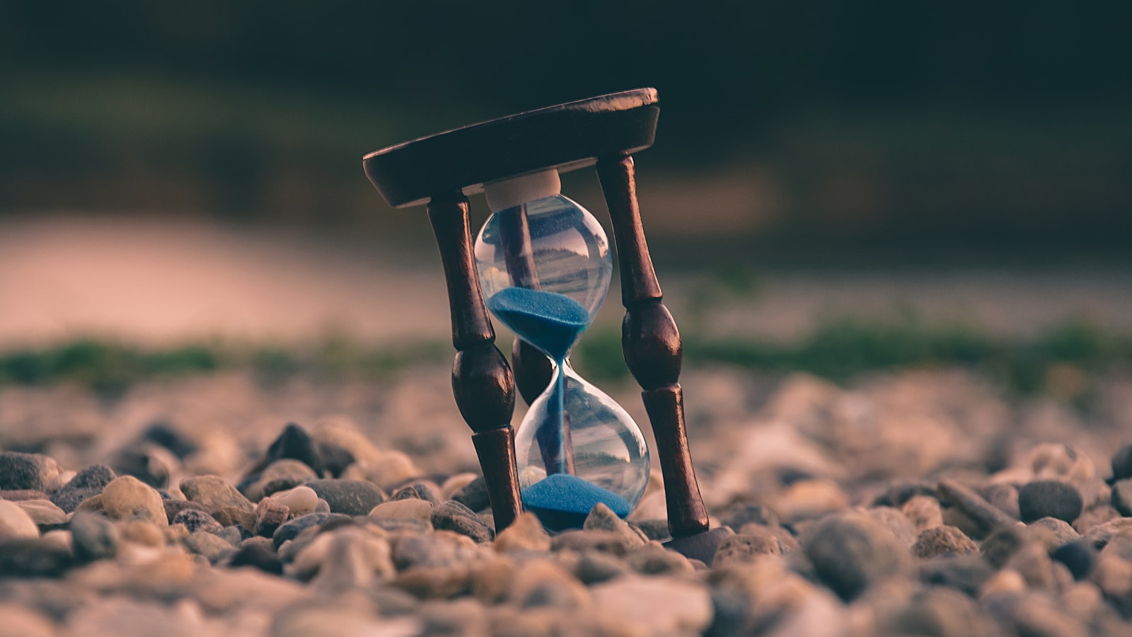 Wooden-frame hourglass with blue sand standing on a bed of smooth river pebbles
