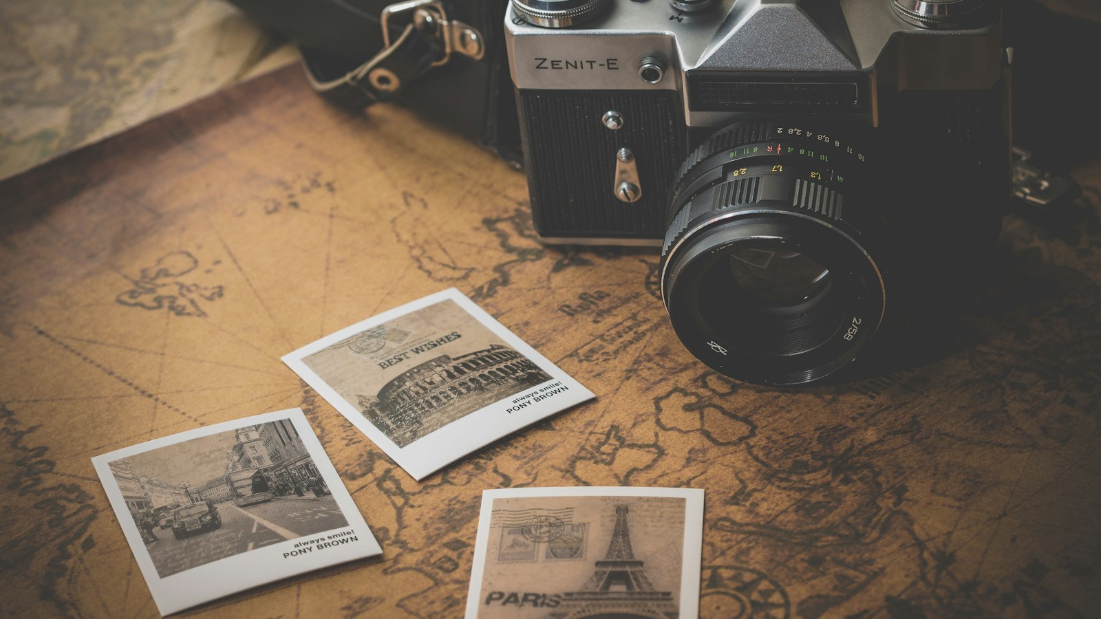 Vintage film camera resting on a wooden table beside scattered photographic prints