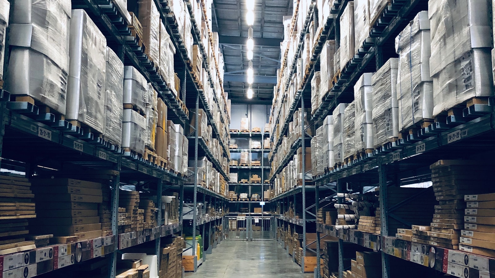 Tall stacks of sealed brown cardboard boxes filling the aisle of a warehouse