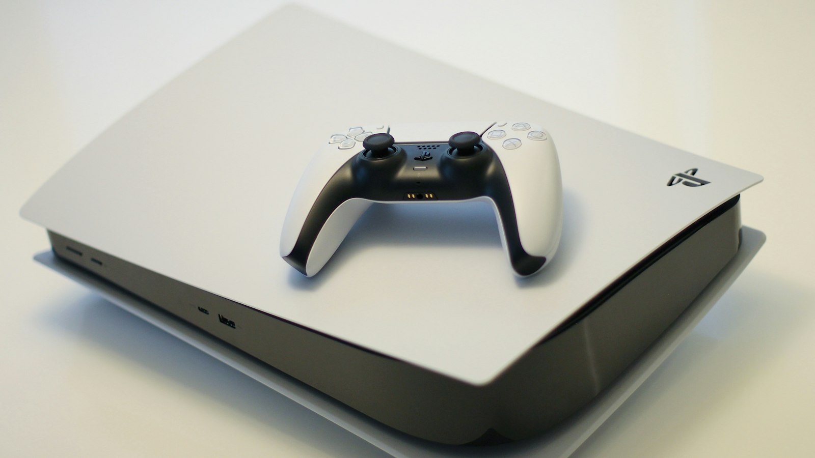 Black video-game controller resting on a desk in front of a glowing screen